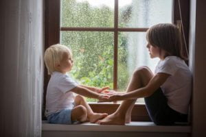 Two siblings hold hands in a window.