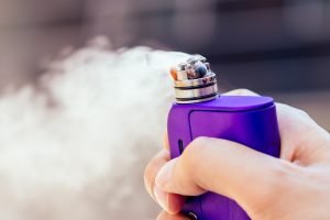 purple vape in a man's hand on a modern background.
