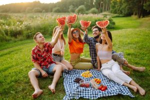 Group of young friends having picnic, eating watermelon, enjoy summer party. Summer vacation concept