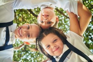Low angle of 3 children hugging together in circle and smiling to camera