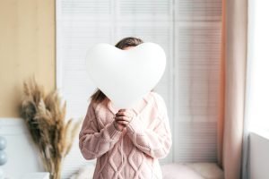 The girl hides her face behind a white balloon heart. Monochrome colors