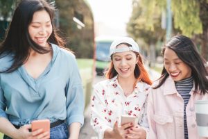 Happy Asian girlfriends walking in the city while watching on mobile smartphones - Young teen girls having fun with new social media apps - Youth millennial generation and technology concept