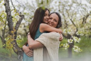 Charming mom and teenage daughter are walking and having fun in the blooming apple garden