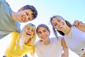 Close-up of happy smiling teenage faces. Hugging teenagers looking at the camera, sky background