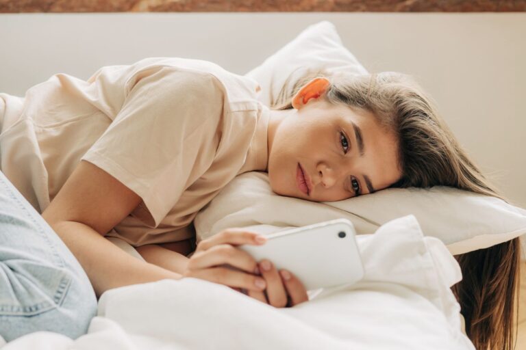 Tired melancholic teenagegirl uses mobile phone while lying in bed