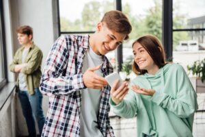 two happy friends smiling while using smartphone in school