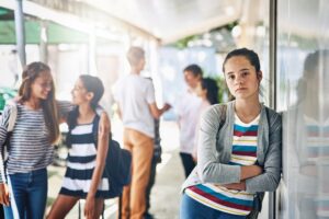 Portrait of a lonely schoolgirl standing outside her classroom with classmates in the background