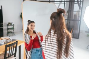 Happy young woman applies makeup on her face in front of the mirror