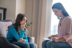 Problems. Long-haired teen in a blue shirt sitting in the psychologists office