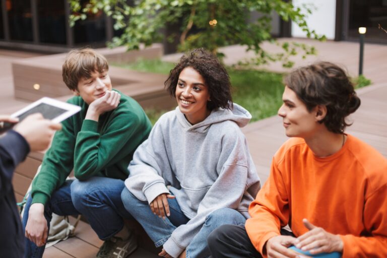 Smiling lady with dark curly hair sitting with her friends in courtyard of university