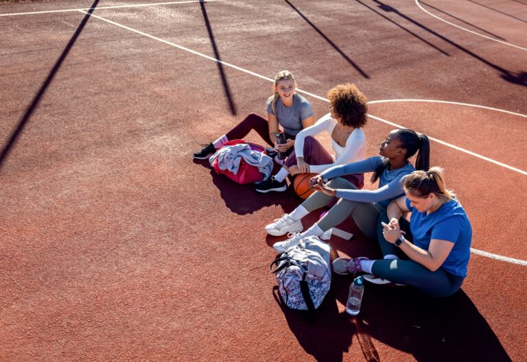 Diverse group of young woman sitting on court resting afrer playing basketball outdoors