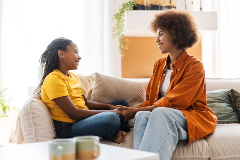 mother and daughter sitting at the sofa and talking while holding hands together