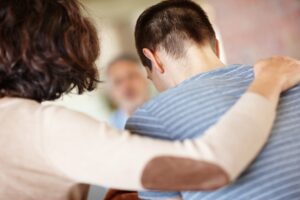 back shot of a mother hugging her teenage son, concept of teenage counseling and therapy