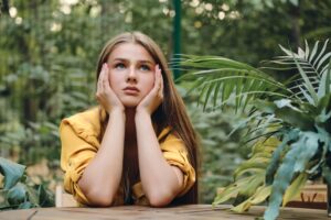 brown haired girl in yellow shirt leaning head on hands looking up among green leaves