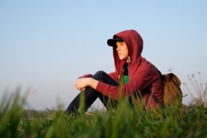 young male teenager sitting outdoors, faraway look symbolizing loneliness, depression, angst